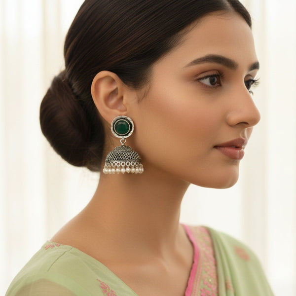 Woman wearing a traditional earring with a green gemstone against a neutral background
