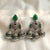 Pair of silver earrings with green and red gemstones on a white fabric background