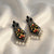 Decorative earrings with black, yellow, and red patterns on a white fabric background