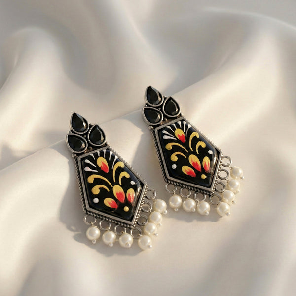 Decorative earrings with black, yellow, and red patterns on a white fabric background