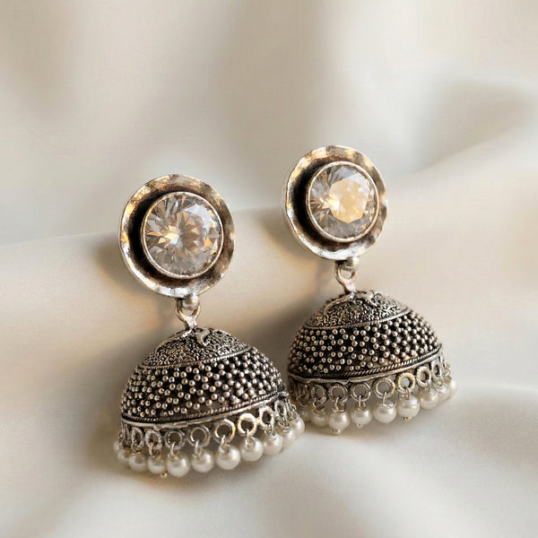 Pair of silver earrings with crystal and pearl details on a soft background