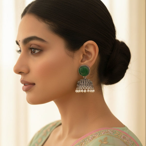 Woman wearing a green and silver earring with a plain background