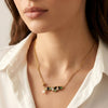 Close-up of gold bar necklace with emerald green stones, black accents, and pearl drop