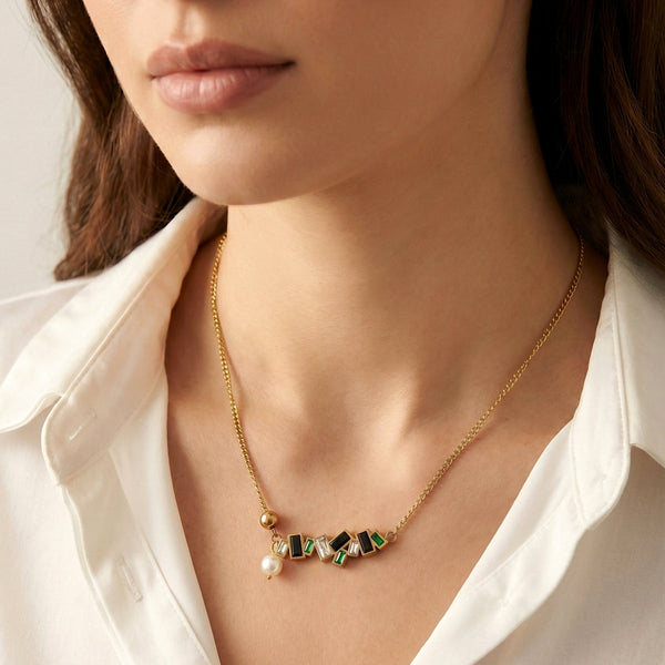 Close-up of gold bar necklace with emerald green stones, black accents, and pearl drop