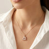 Close up of heart shaped gold pendant with pink center stone and crystal detailing by Evvara Vogue