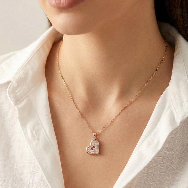 Close up of heart shaped gold pendant with pink center stone and crystal detailing by Evvara Vogue